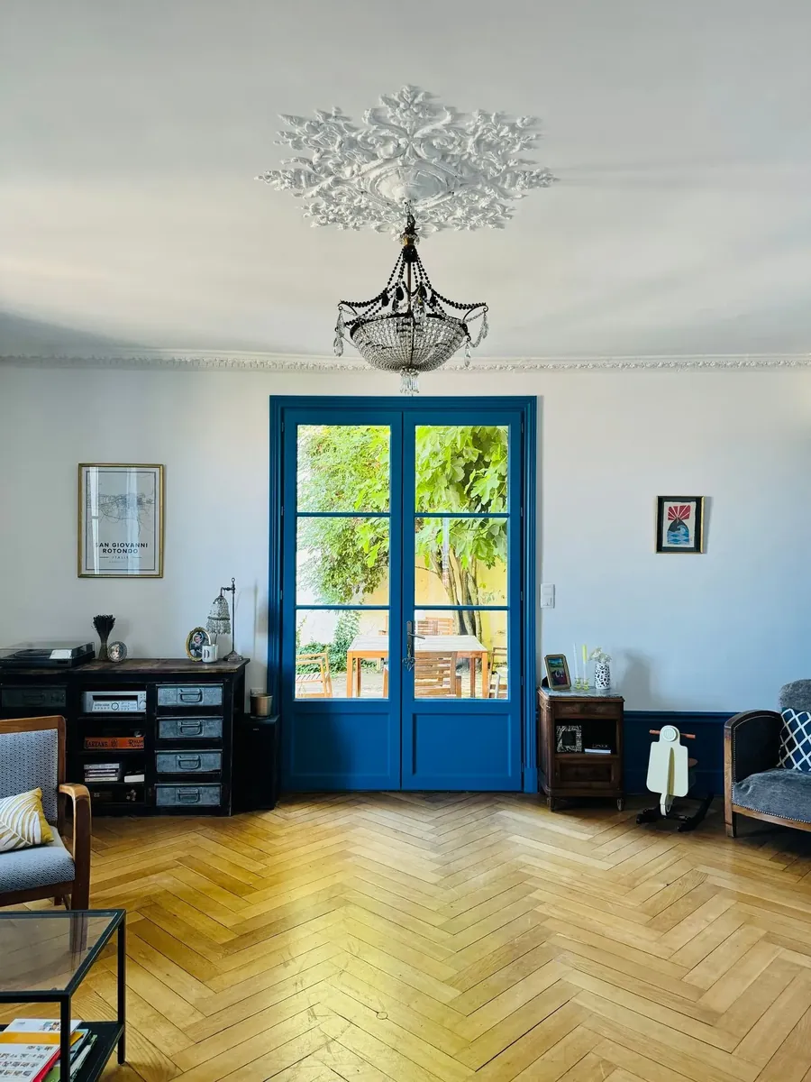 Salon aux murs et au plafond peints, avec rosace au plafond, portes-fenêtres bleues et parquet en chevrons
