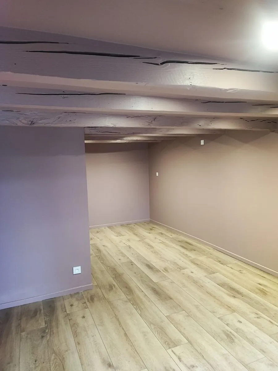 Pièce vide aux murs mauves et poutres apparentes, sol en lames PVC posées droit